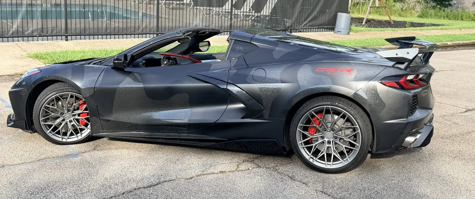 Side profile of a C8 Corvette with a gray camo wrap, red brake calipers and a rear wing
